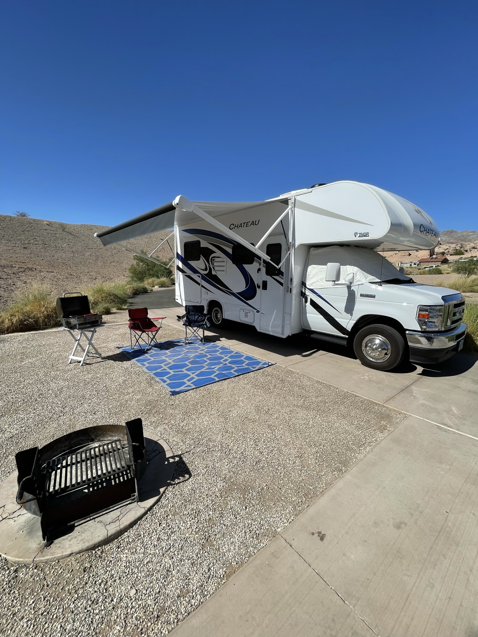 2022 Thor Chateau Class C RV parked at a Las Vegas campsite with awning extended, camping chairs, grill, and outdoor rug set up.