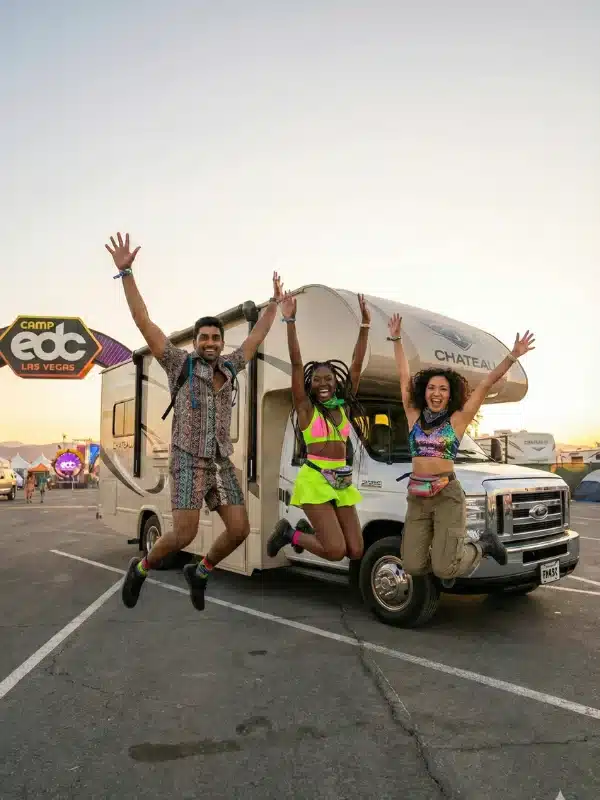Three excited friends in front of an RV at camp edc